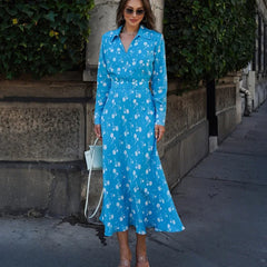 Woman wearing a blue floral dress standing outdoors with greenery in the background