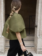 Woman wearing a green cape walking through an architectural entrance.