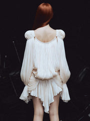 Person wearing a white dress with puffed sleeves and a high-low hemline on a dark background