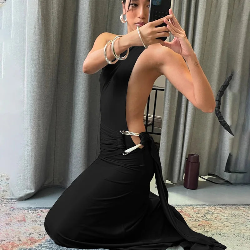 Woman in a black dress taking a mirror selfie in a room with gray curtains.