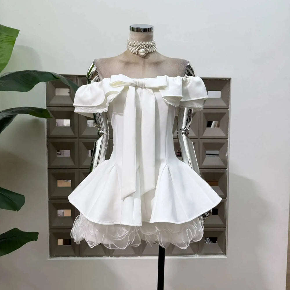 Detail of the off-shoulder neckline and bow on the white mini dress