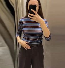 Person taking a mirror selfie wearing a striped shirt and dark pants.