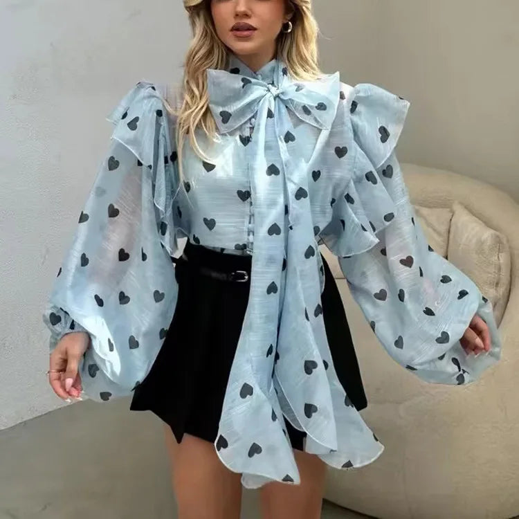 Woman wearing a light blue blouse with black heart patterns and a large bow, paired with a black skirt.