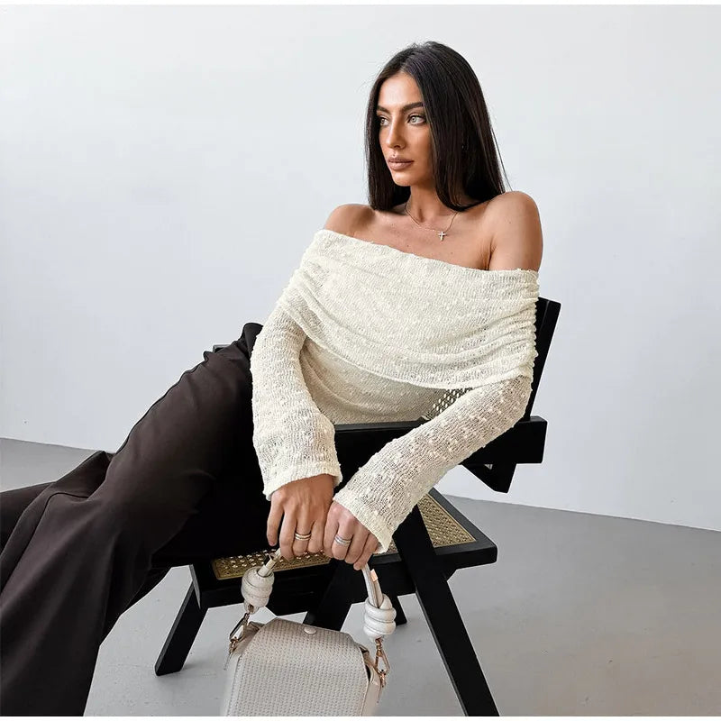 Woman wearing a white off-shoulder sweater sitting on a chair with a plain background