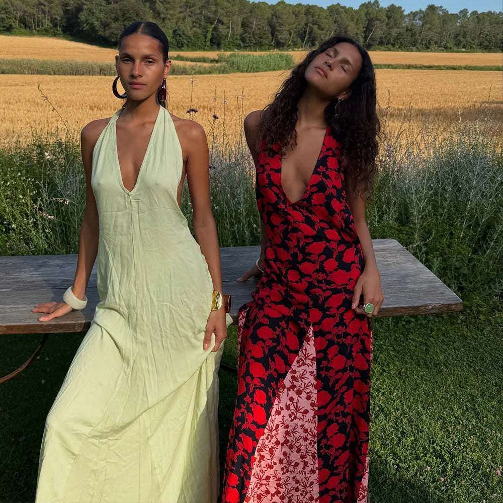 Two women in dresses sitting on a bench in a field.