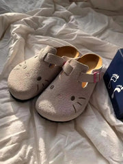 Light grey Hello Kitty flat mule slippers with pink buckle straps on a white textured surface.