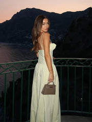 Woman in a white dress holding a handbag, standing on a balcony with a mountainous background.