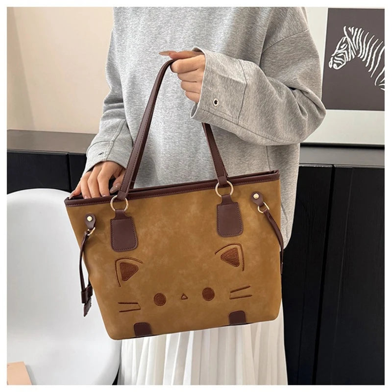 Person holding a brown suede-like tote bag with a cat face design