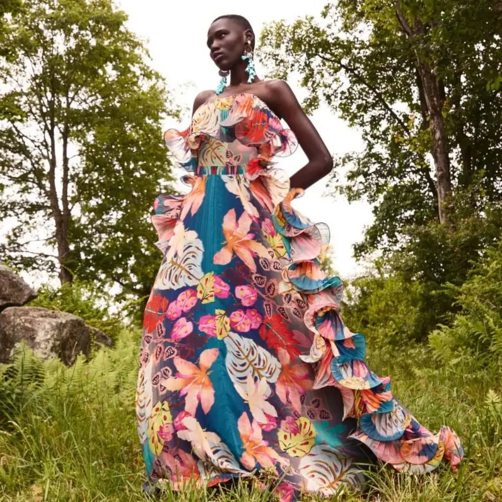 Tropical print one-piece swimsuit with ruffled skirt worn by a model in an outdoor setting.