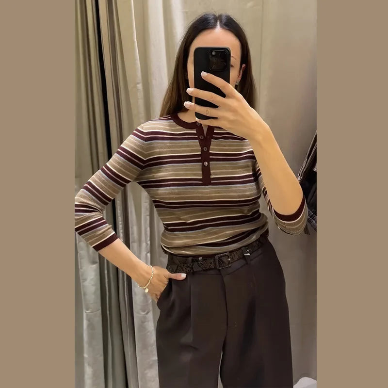 Person wearing a striped sweater and dark pants taking a mirror selfie.