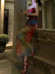 Woman in a colorful dress standing against a stone wall.