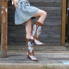 Person wearing cowboy boots with colorful designs sitting on a wooden bench.