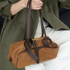 Brown handbag held by a person wearing a green coat and white pants.