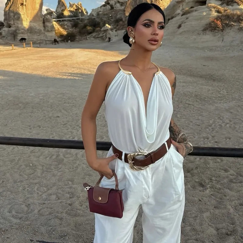Woman in a white outfit with a brown belt and red handbag standing on a sandy landscape.