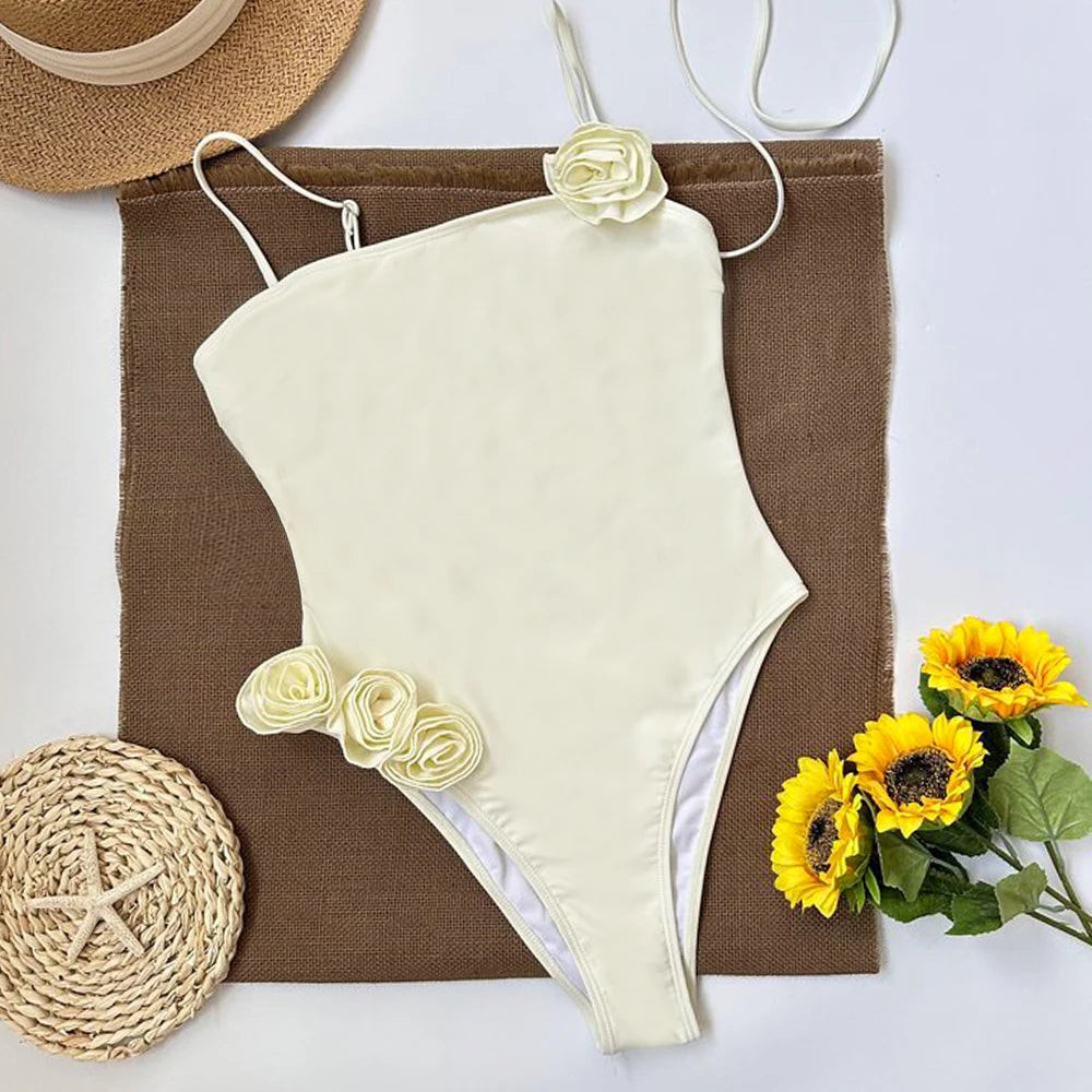 Flat lay of a cream one piece swimsuit with rosette details, surrounded by beach accessories.