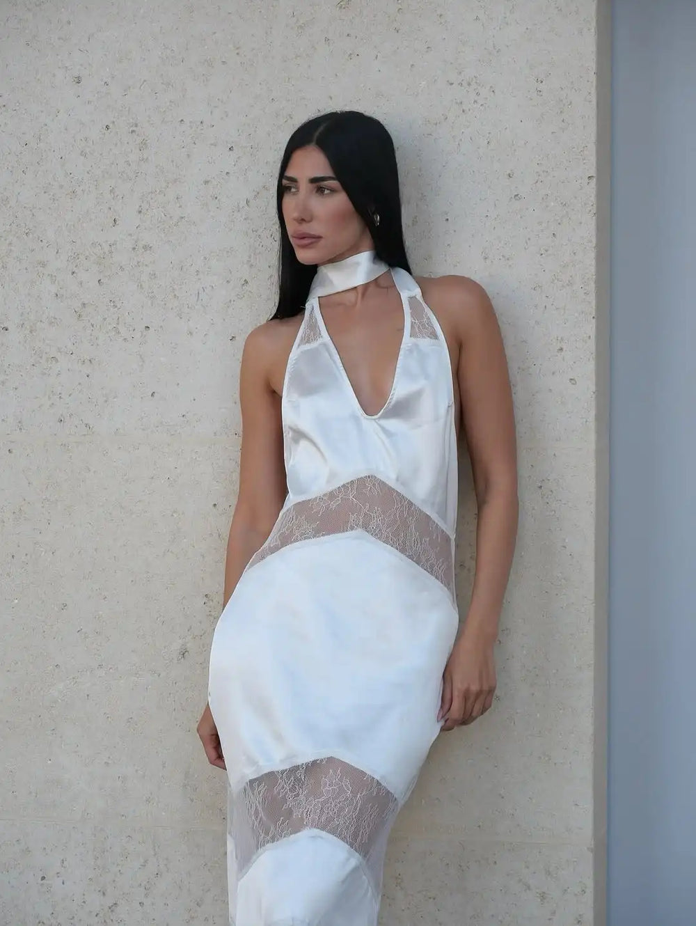 Woman wearing a white dress with lace details against a light-colored wall.