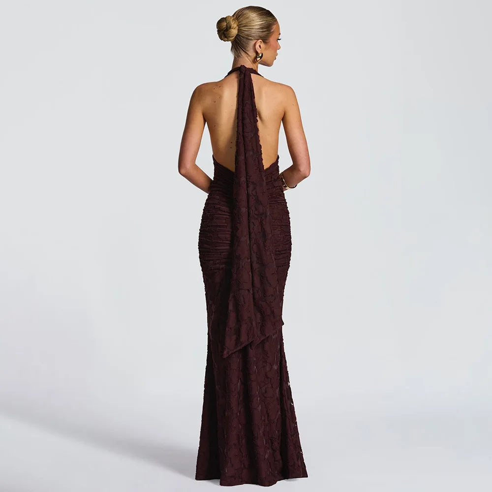 Woman wearing a burgundy evening gown with a halter neck and open back on a light gray background
