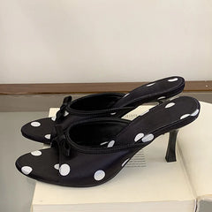 Black polka dot heeled mules with a black bow on a table