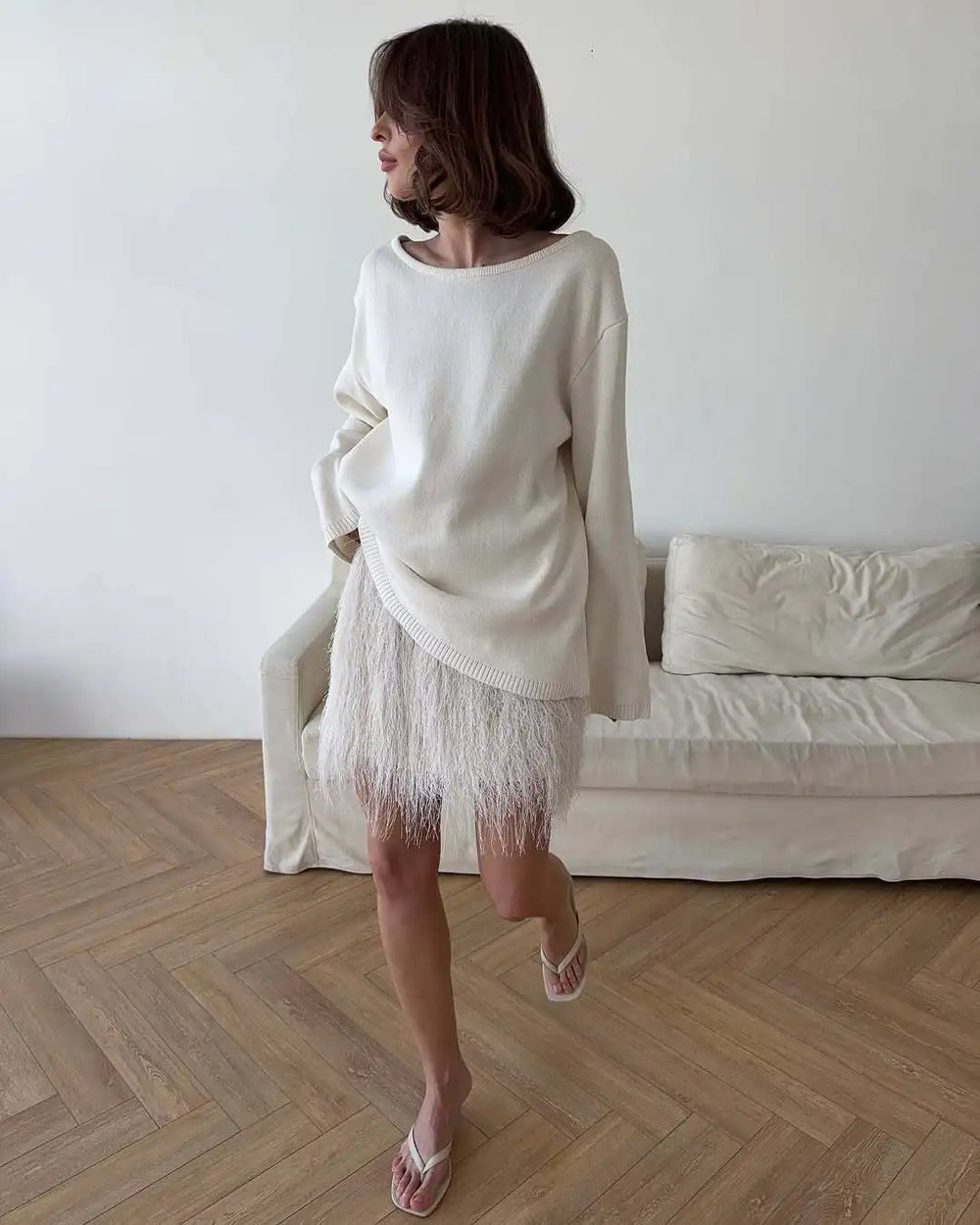 Woman wearing a beige sweater and skirt standing in a room with a white couch.