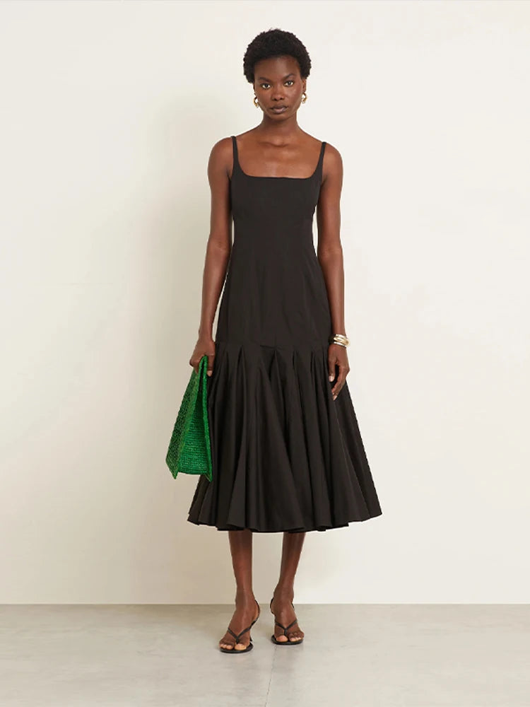 Woman wearing a black dress holding a green clutch against a white background