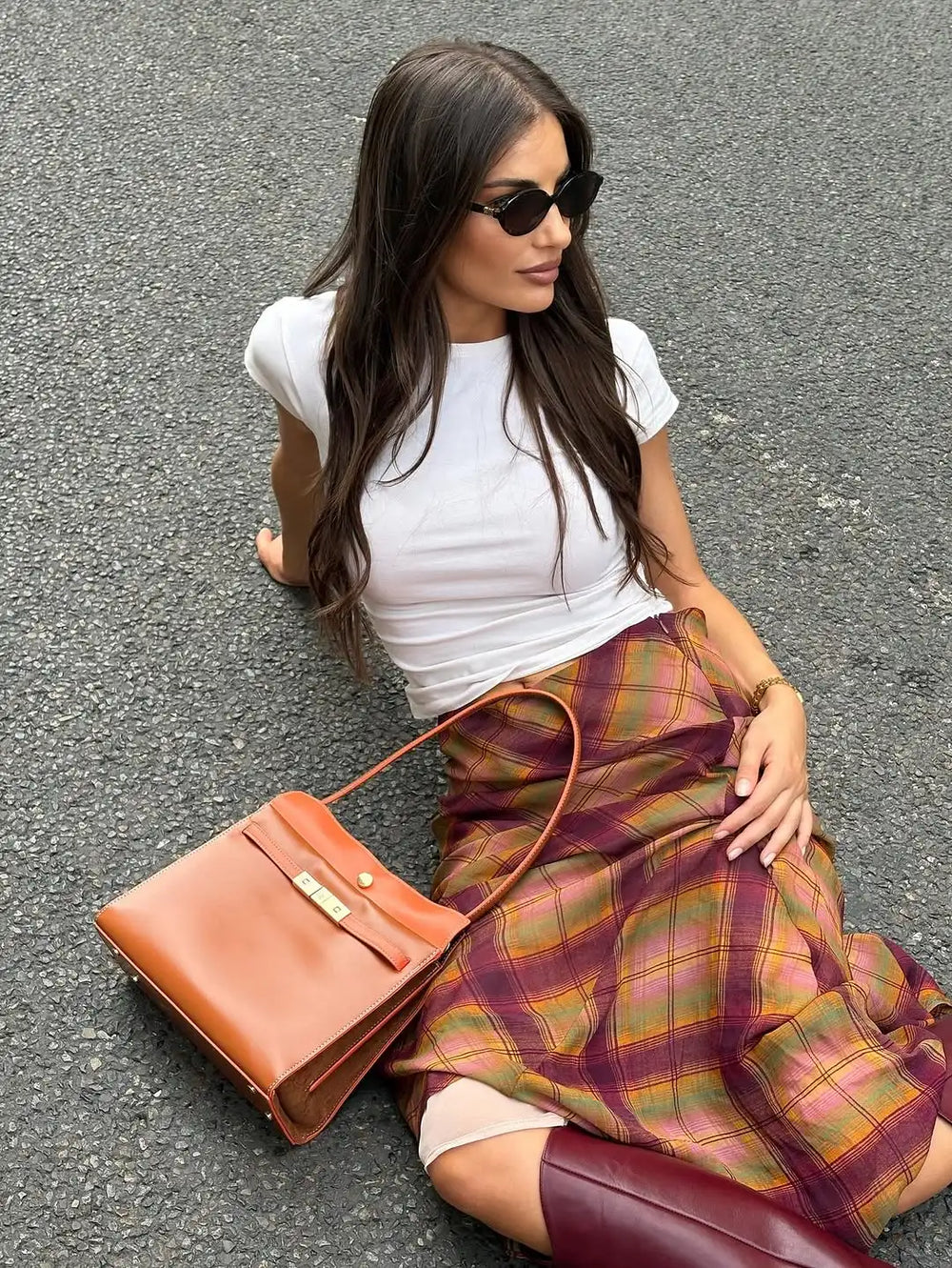 Woman sitting on the ground wearing an irregular hem plaid maxi skirt and a white t-shirt.
