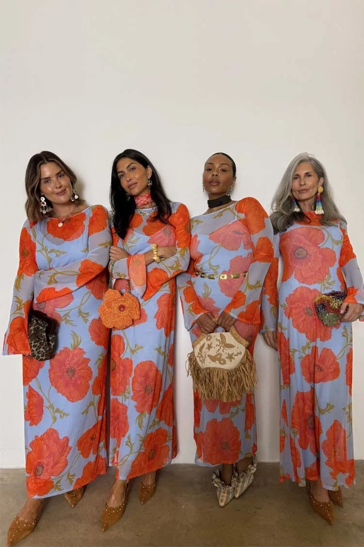 Four women wearing matching floral dresses posing against a white wall.