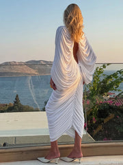 Woman in a white dress standing by a scenic view of water and mountains.