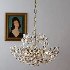 A crystal chandelier hangs against a gray wall with a framed portrait in the background.