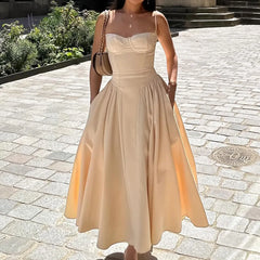 Woman wearing a beige dress standing on a stone pavement with greenery in the background