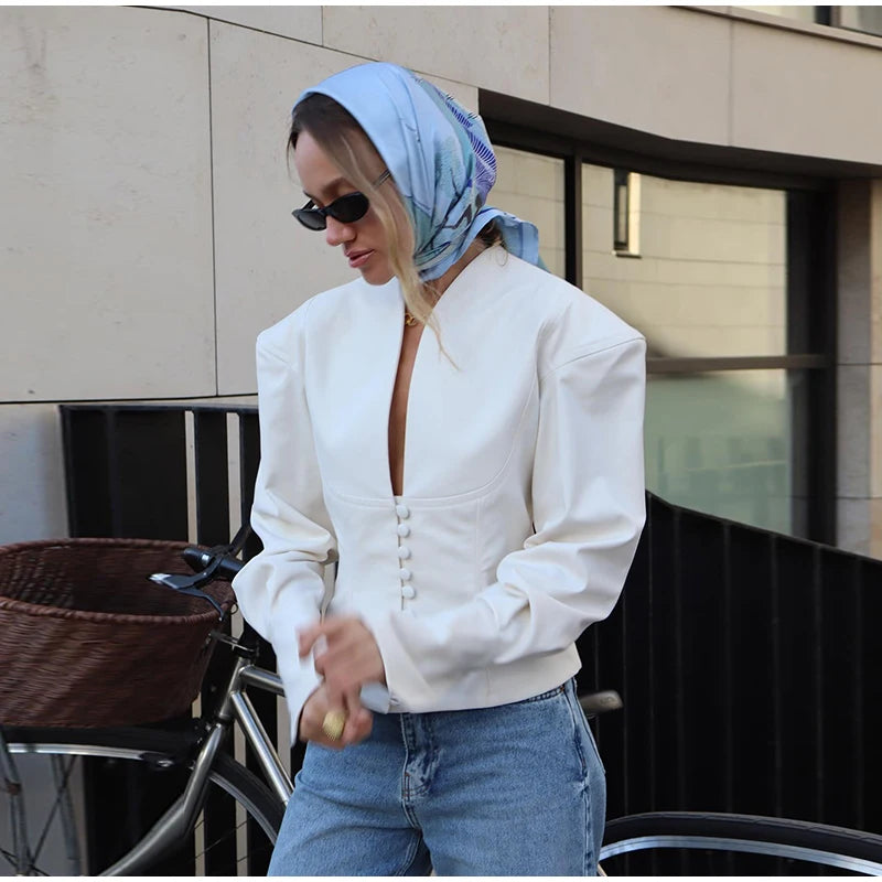 Woman wearing a white jacket and blue jeans with a headscarf, standing outdoors.