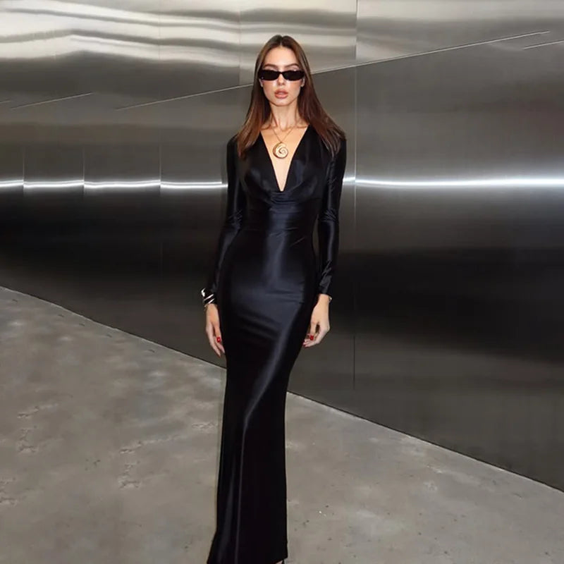 Woman in a black satin dress standing against a reflective metallic wall.