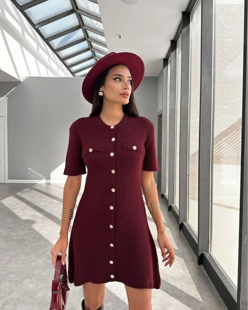 Woman wearing a burgundy dress and hat in a modern hallway.
