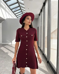 Woman wearing a burgundy dress and hat in a modern hallway.
