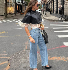 Woman in stylish outfit with black top, white shirt, blue jeans, and black shoes on a city street.