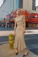Woman in a polka dot dress standing on a city street with a colorful theater marquee in the background.