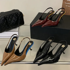 Set of heeled shoes in various colours on a reflective surface with a black handbag in the background