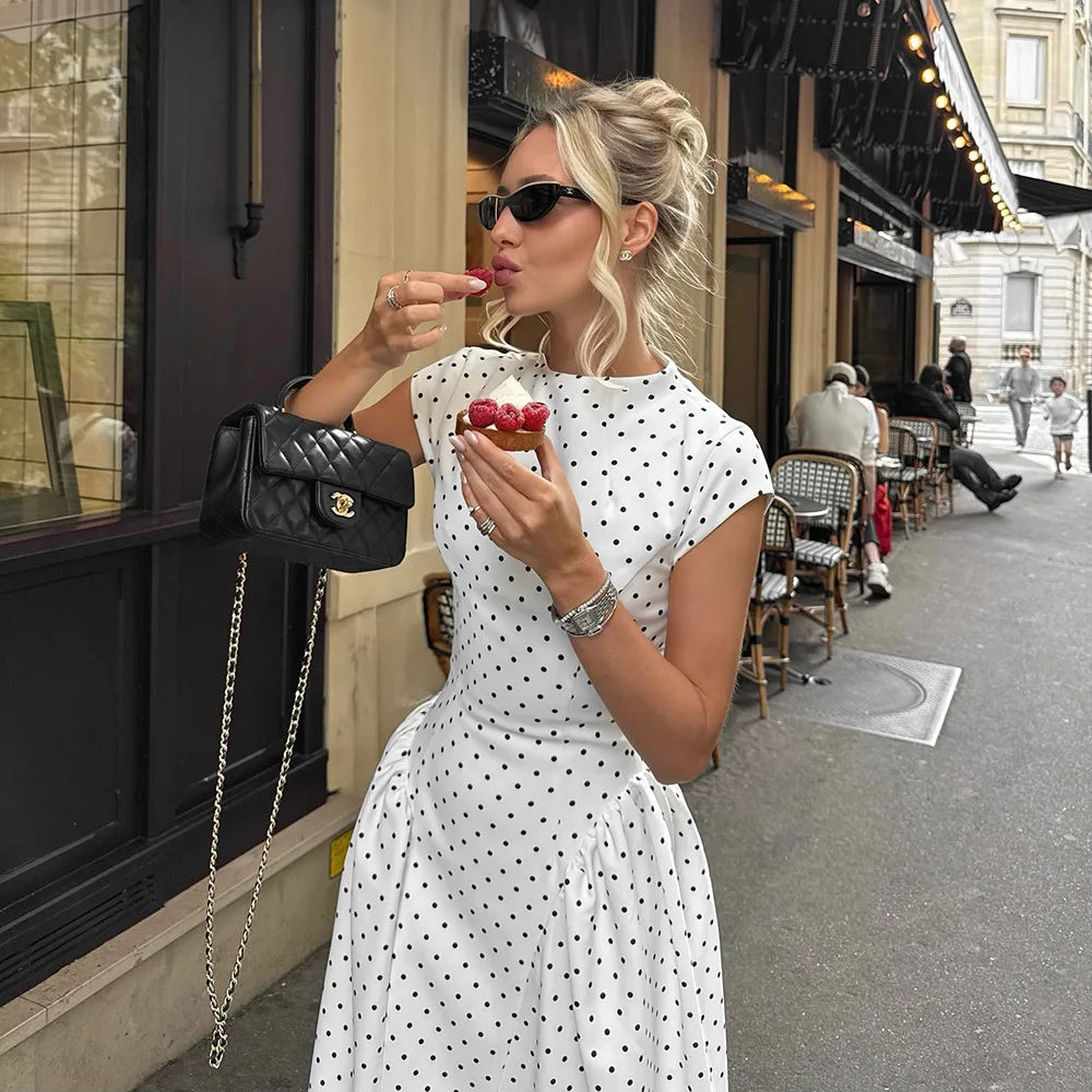 Woman in a polka dot dress eating ice cream on a city street.