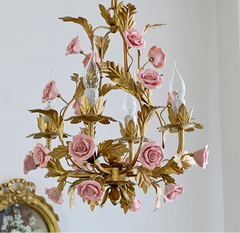 Gold chandelier with pink roses against a light gray wall