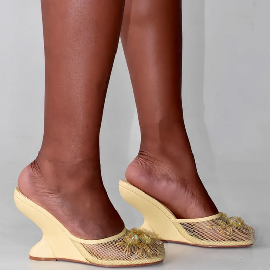 Yellow mesh wedge mules with floral embellishments on foot