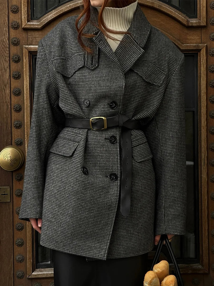 Person wearing a gray checkered coat standing in front of a wooden door.