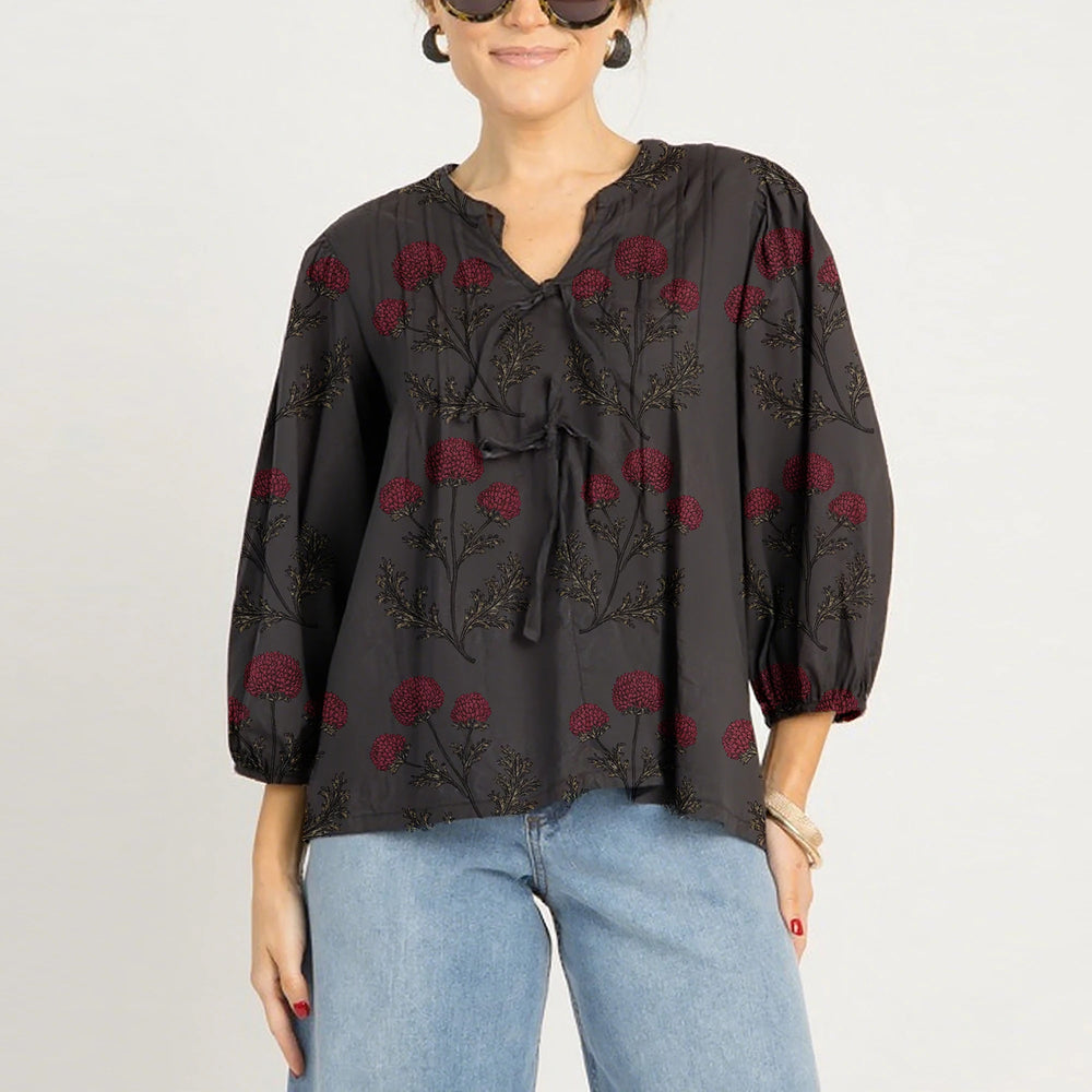 Woman wearing a black blouse with red floral embroidery and blue jeans on a light gray background