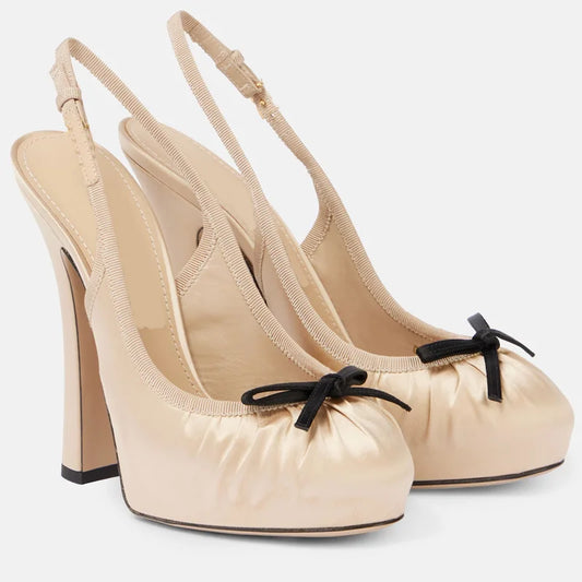 Beige satin slingback platform pumps with a black bow detail.