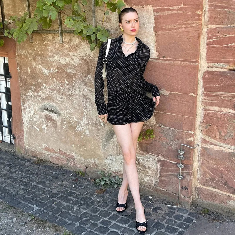 Woman in a black outfit standing against a textured wall.