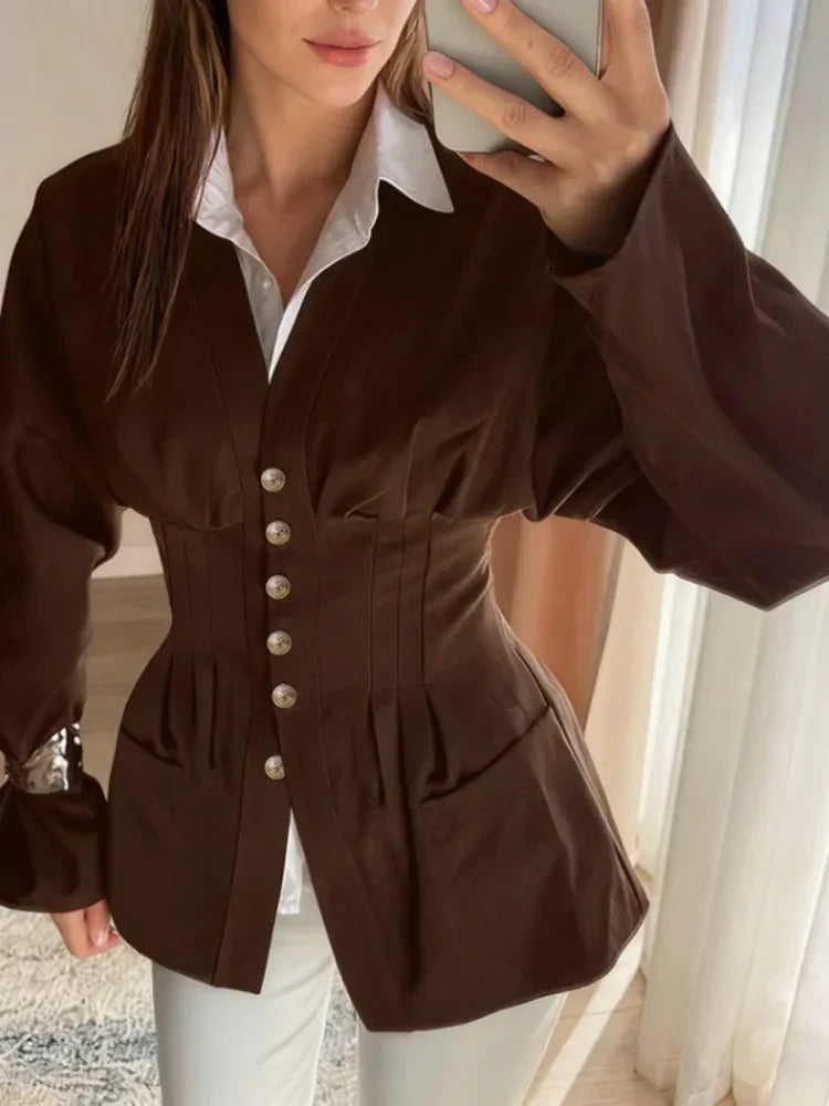 Person wearing a brown jacket with a white shirt underneath, taking a mirror selfie.