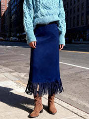 Person wearing a blue sweater, navy skirt with fringe, and brown boots on a city street.