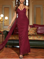 Woman in a burgundy evening gown standing in an elegant room with a couch and lamp.