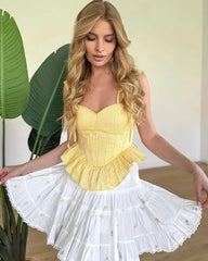 Woman wearing a yellow top and white skirt with ruffled layers, standing indoors.