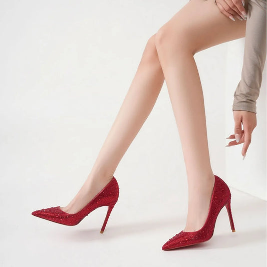 Red high-heeled shoes with rhinestone details worn by a person 