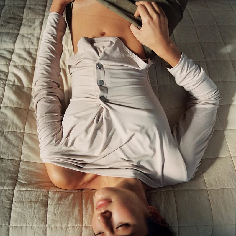 Person lying on a bed with a white shirt partially pulled up, wearing a skirt.