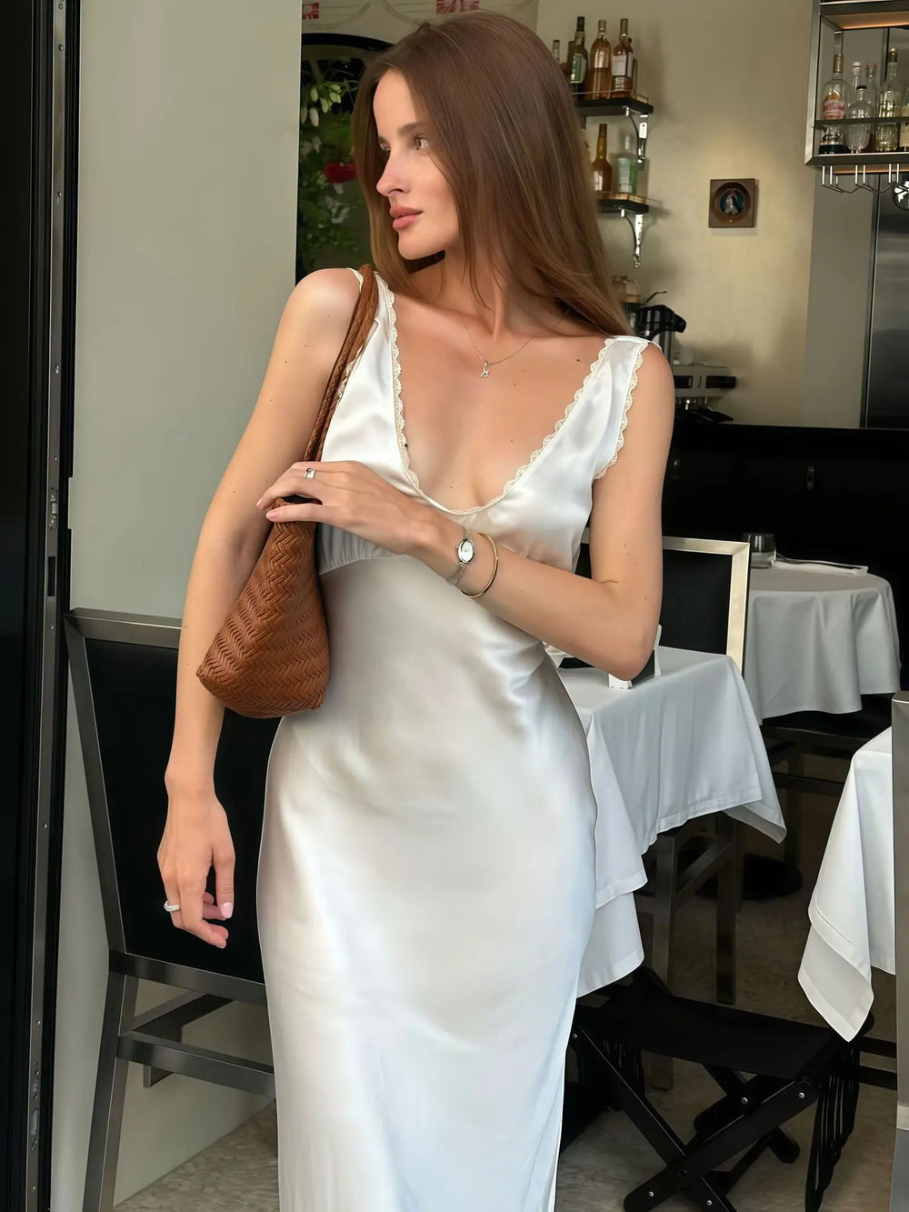 Woman in a white satin dress holding a brown handbag in a restaurant setting